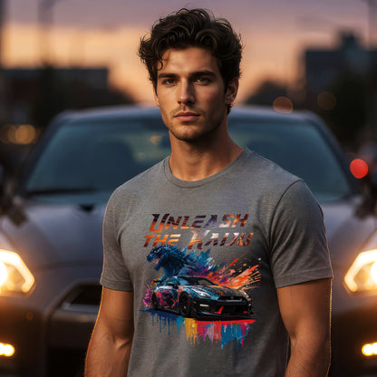 Man wearing a gray t-shirt with nissan gtr35 with godzilla design and text 'UNLEASH THE KAiju'  standing in front of cars at dusk.